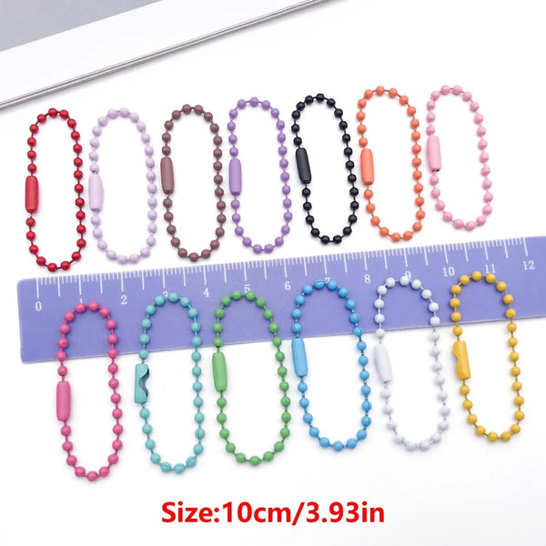 A collection of colorful metal ball bead chains of various colors and sizes laid out next to a ruler.