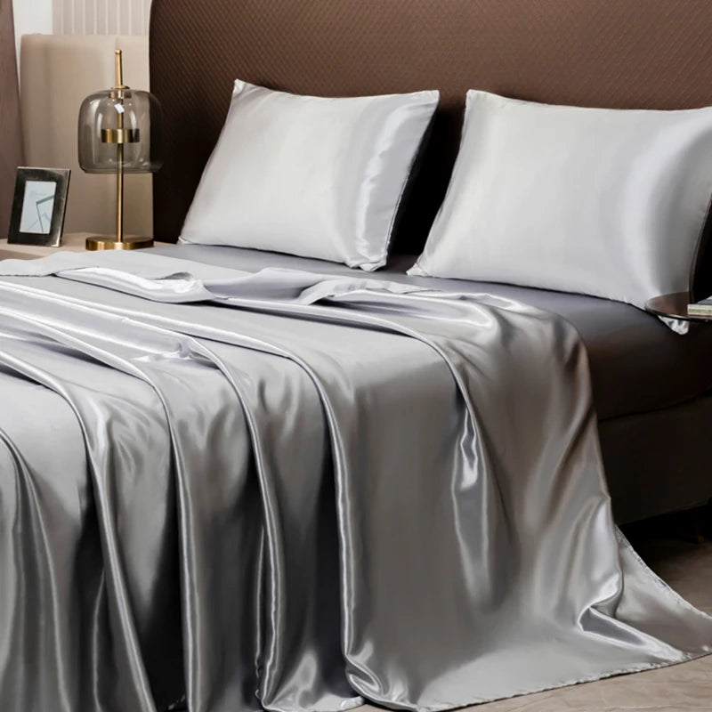 A luxury solid satin bedding set featuring silver gray sheets and pillows on a bed.