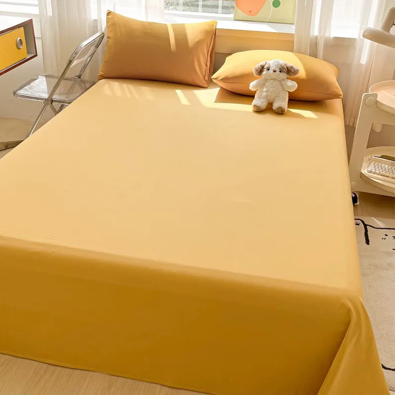 A bright yellow organic cotton bedding set featuring a flat sheet, pillows, and a small stuffed animal on a bed.