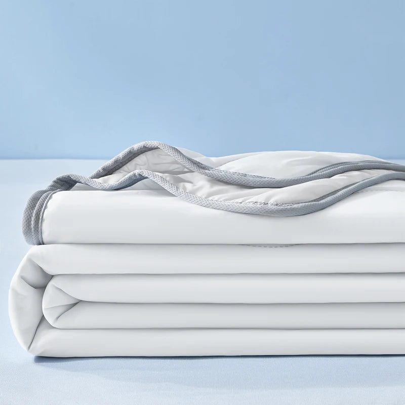 A stack of white cooling fiber blankets with light gray fabric draped on top against a pale blue background.