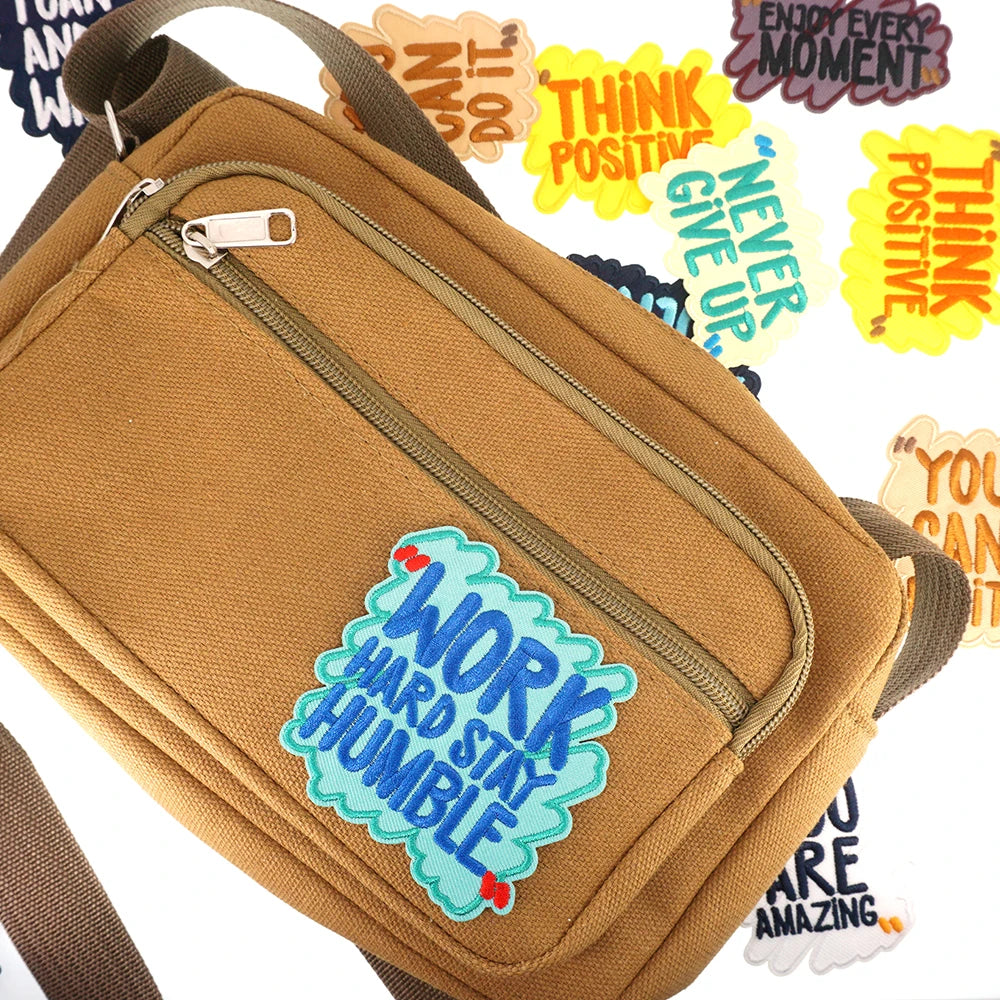 A tan canvas iron-on patch bag with a zipper and various motivational text patches