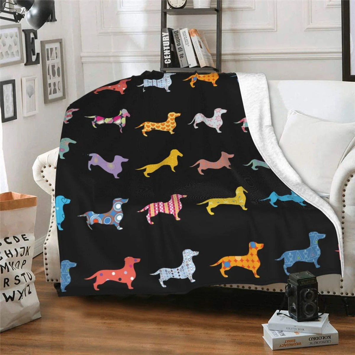 A black flannel blanket featuring various colorful dachshund silhouettes on a white sofa.