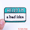 An embroidered patch with the text HELLO I'M a bad idea on a teal and white background.
