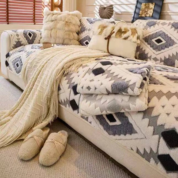 A beige and gray patterned fleece sofa slipcover with faux fur pillows and a long cream throw blanket.