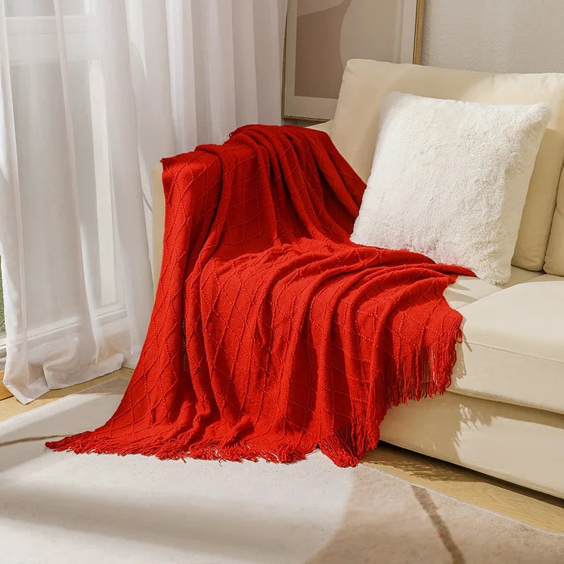A vibrant red knitted tassel throw blanket draped over a light-colored sofa.