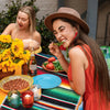 A woman laughing while eating a tomato and herb on a colorful striped table runner.