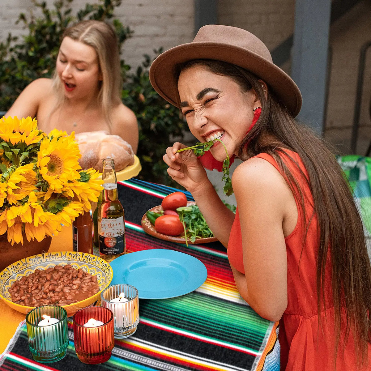A woman laughing while eating a tomato and herb on a colorful striped table runner.
