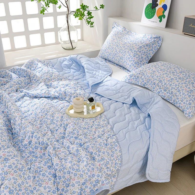 Light blue floral quilted quilt set with matching pillows displayed on a white bed.