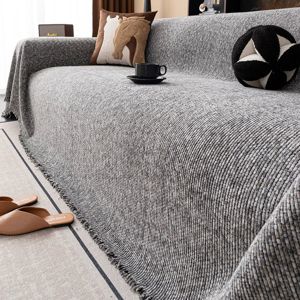 A gray chenille sofa cover draped over a sofa, with decorative pillows and a mug on the surface.