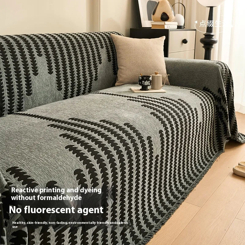 Gray and black reactive printed chenille sofa cover with tassel fringes draped over a bed.