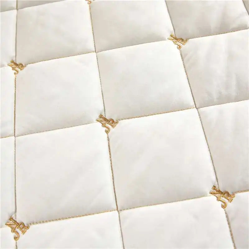 White quilted bed skirt featuring gold embroidery on a square pattern.