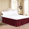 A white bed with a deep maroon ruffle skirt and a light beige headboard in a bright room.