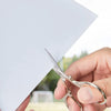 A hand holds a pair of premium stainless steel embroidery scissors poised over a white piece of fabric.