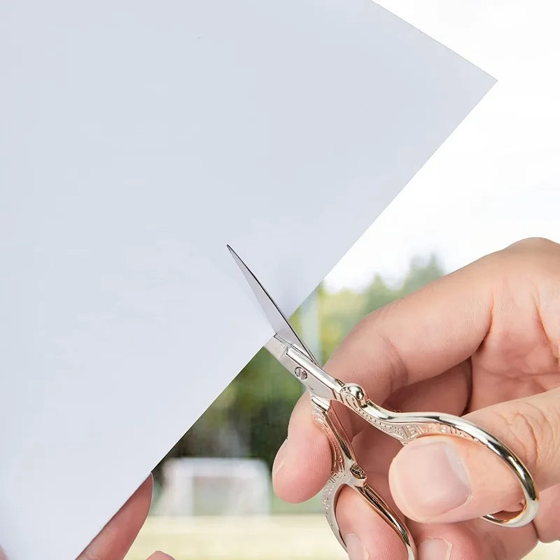 A hand holds a pair of premium stainless steel embroidery scissors poised over a white piece of fabric.