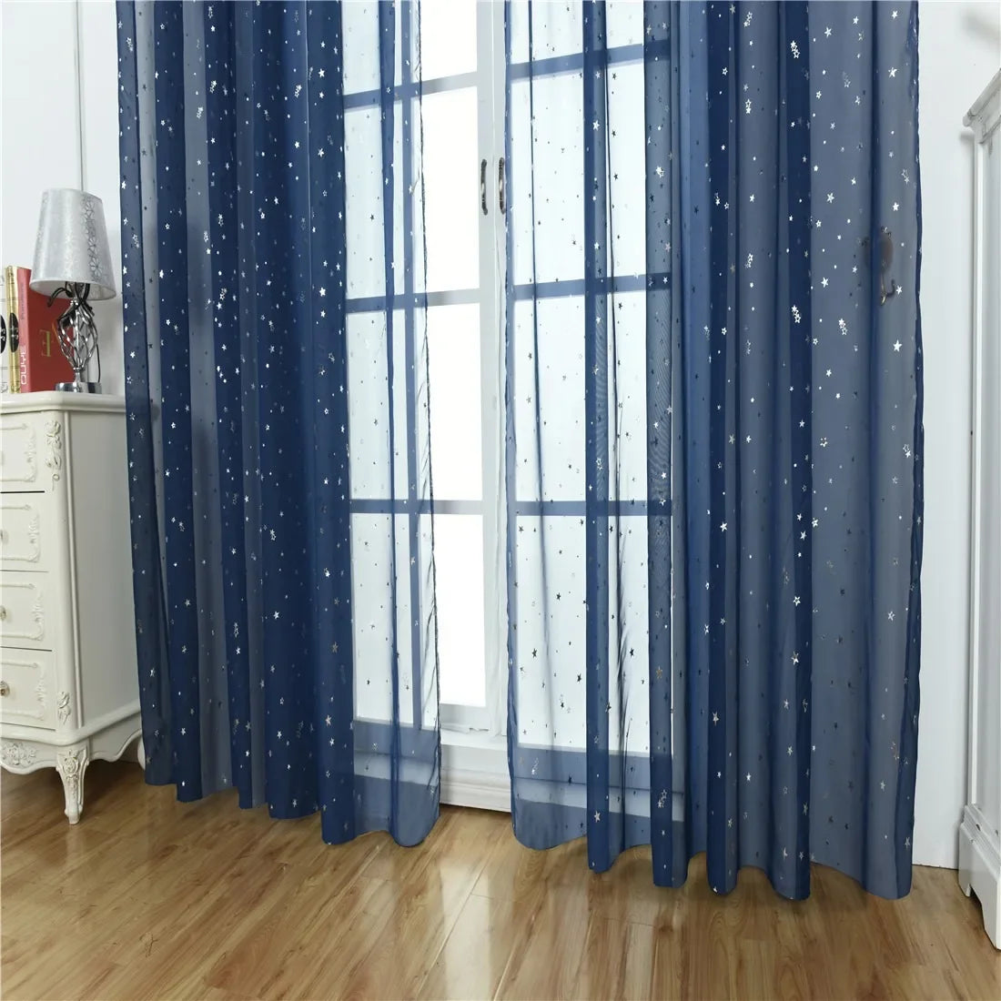 Blue sheer curtains with silver star patterns hanging in a window.