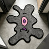 A playful one-eye monster area rug with a gray body and pink eye on a light floor.