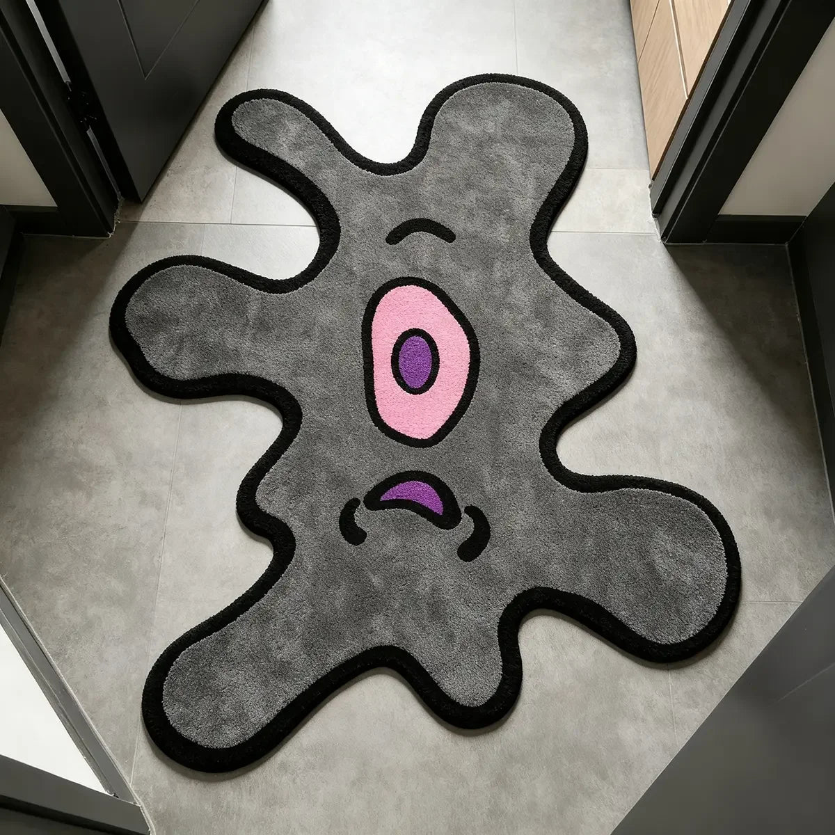 A playful one-eye monster area rug with a gray body and pink eye on a light floor.