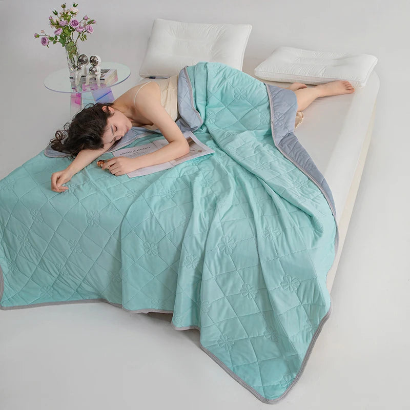 A woman is lying on a light blue quilted blanket, looking relaxed, with a white pillow and some flowers nearby.