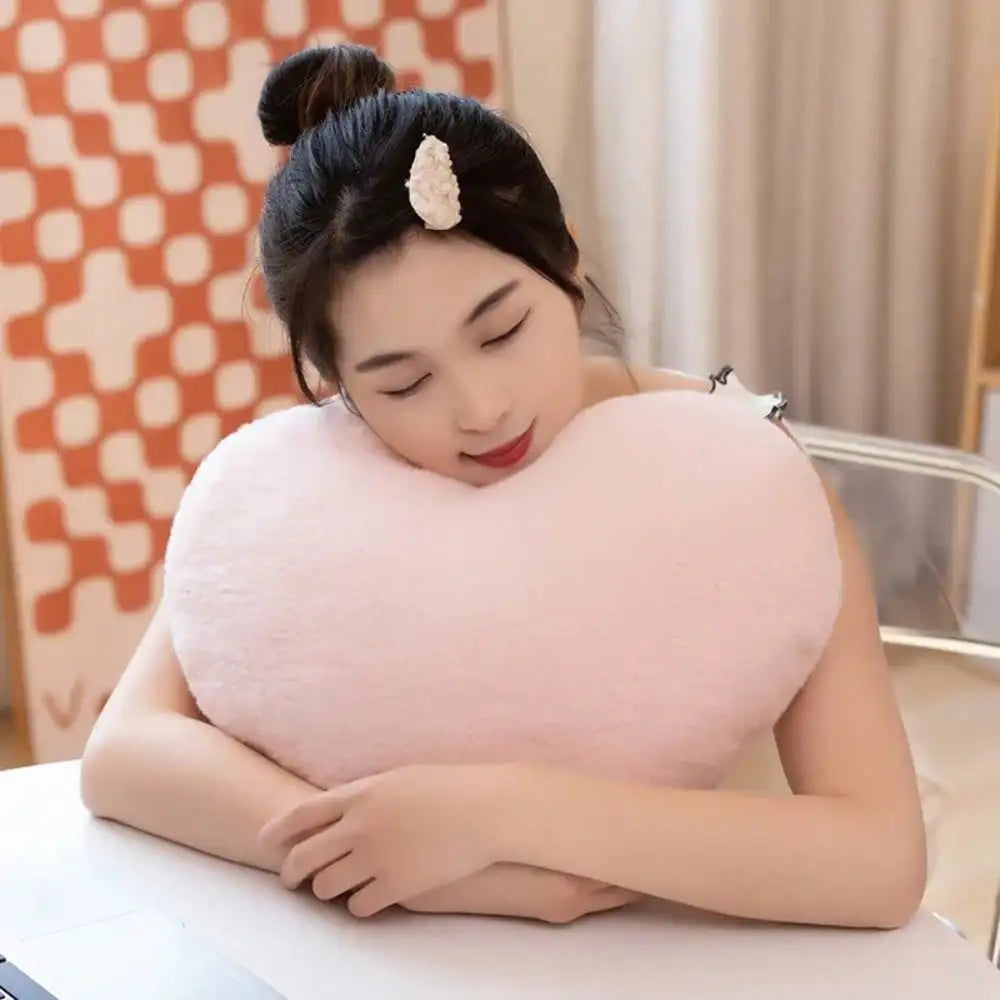 A woman rests her head on a pink heart-shaped plush cushion.