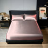 A pink satin bedding set with two pillows is displayed on a black bed frame in a modern bedroom setting.