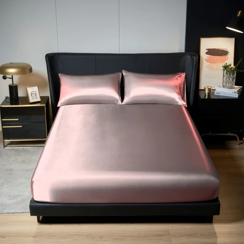 A pink satin bedding set with two pillows is displayed on a black bed frame in a modern bedroom setting.