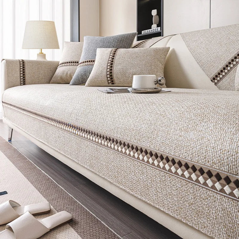 A beige linen sofa cover with decorative trim and pillows on a light-colored sofa in a modern living room.