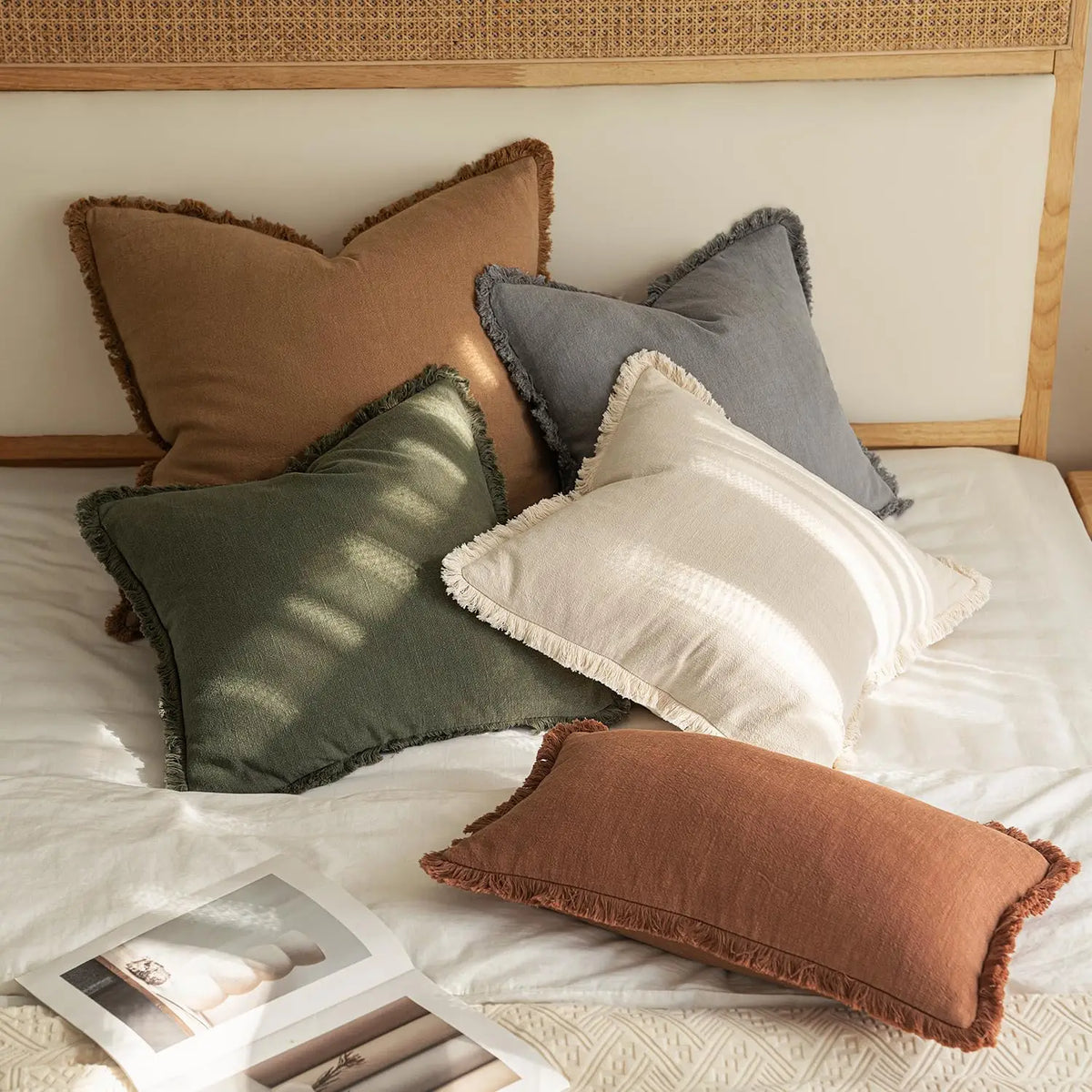 A collection of linen fringe throw pillow covers in earthy tones like olive green, terracotta, and gray resting on a white be