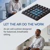 A gray-skinned man sits on a black air-cell cushion designed for balanced, breathable sitting.