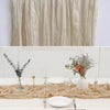 A close-up of a beige semi-sheer gauze table runner draped over a white tablecloth with place settings.