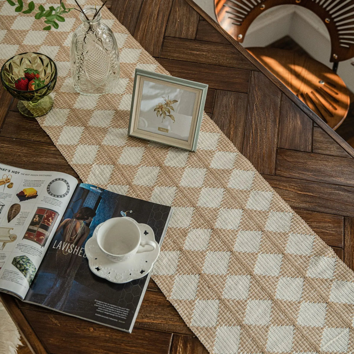 A boho farmhouse linen table runner laid on a dark wood surface with a framed picture and glass vase.