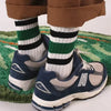 A pair of men's retro striped crew socks worn by a person, paired with athletic shoes and brown pants.