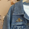 A close-up of a denim jacket featuring an embroidered colorful moth patch on the chest.