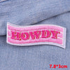 Pink embroidered letter patch spelling HOWDY sewn onto a blue denim fabric.