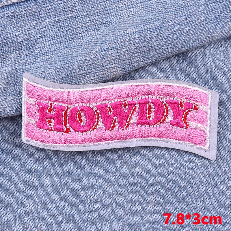 Pink embroidered letter patch spelling HOWDY sewn onto a blue denim fabric.