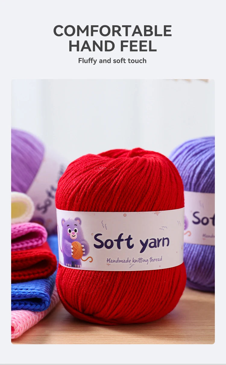 A bright red ball of soft yarn is shown next to other colored yarns on a wooden surface.