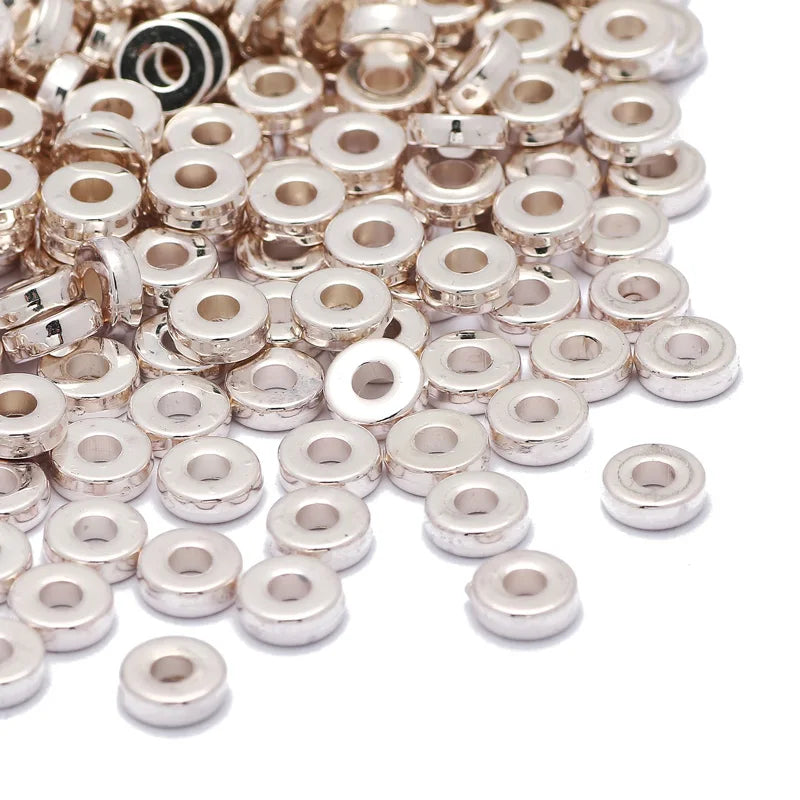 A pile of small, silver-toned acrylic flat round spacer beads for DIY jewelry.