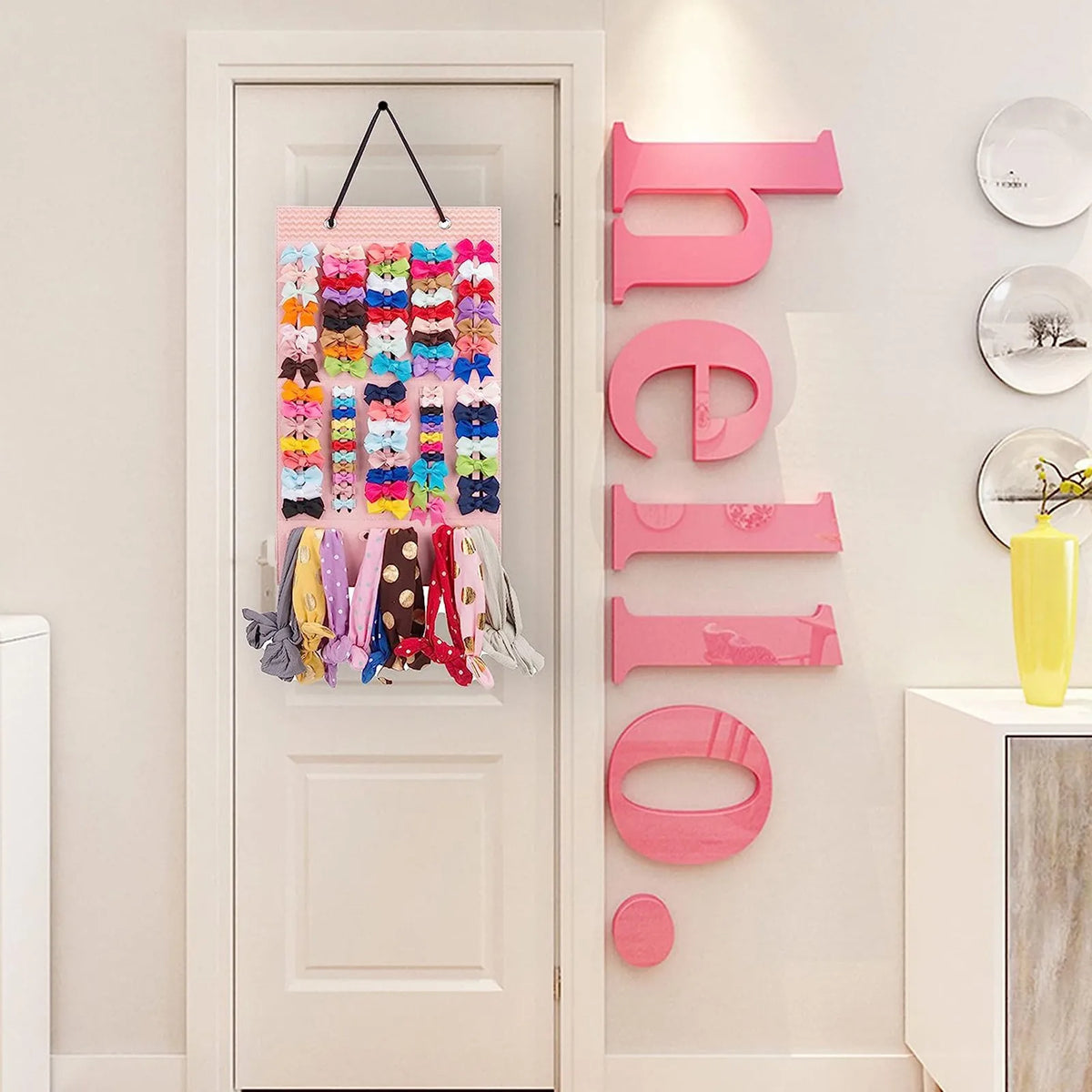 A pink and multicolored hair clip storage hanger with various colored clips displayed on a white door and mounted on a wall.