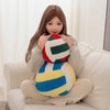 A woman is holding a yellow and blue plush volleyball ball cushion against her chest while sitting on a light-colored sofa.