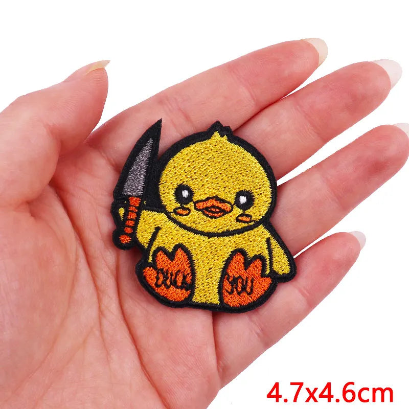 A yellow embroidered cartoon chick with a knife, shown in a person's hand.