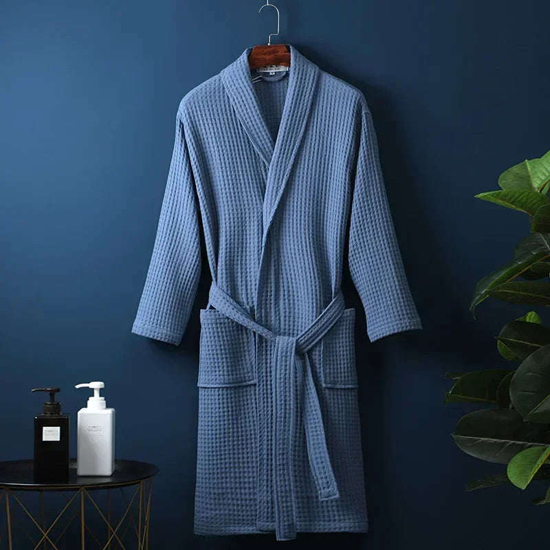 A light blue cotton terry robe hanging on a dark blue wall next to skincare products.