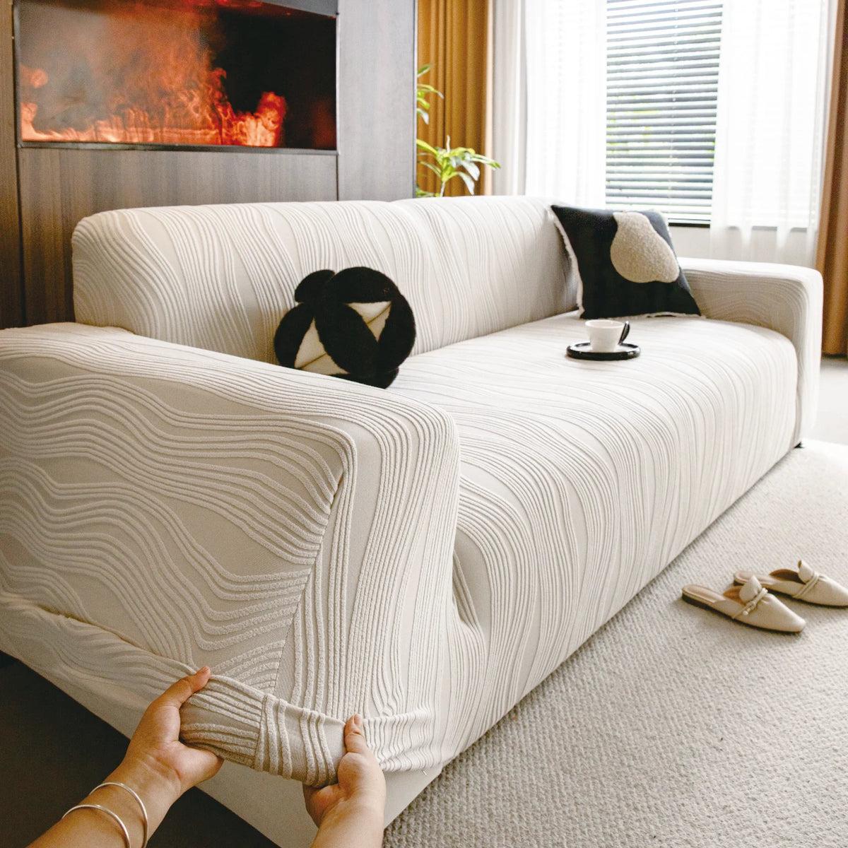 A cream-colored stretchable sofa cover with a vertical line pattern is shown on a light rug.