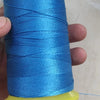 A spool of bright blue high tenacity polyester sewing thread is held in a hand, with a yellow plastic cap visible.