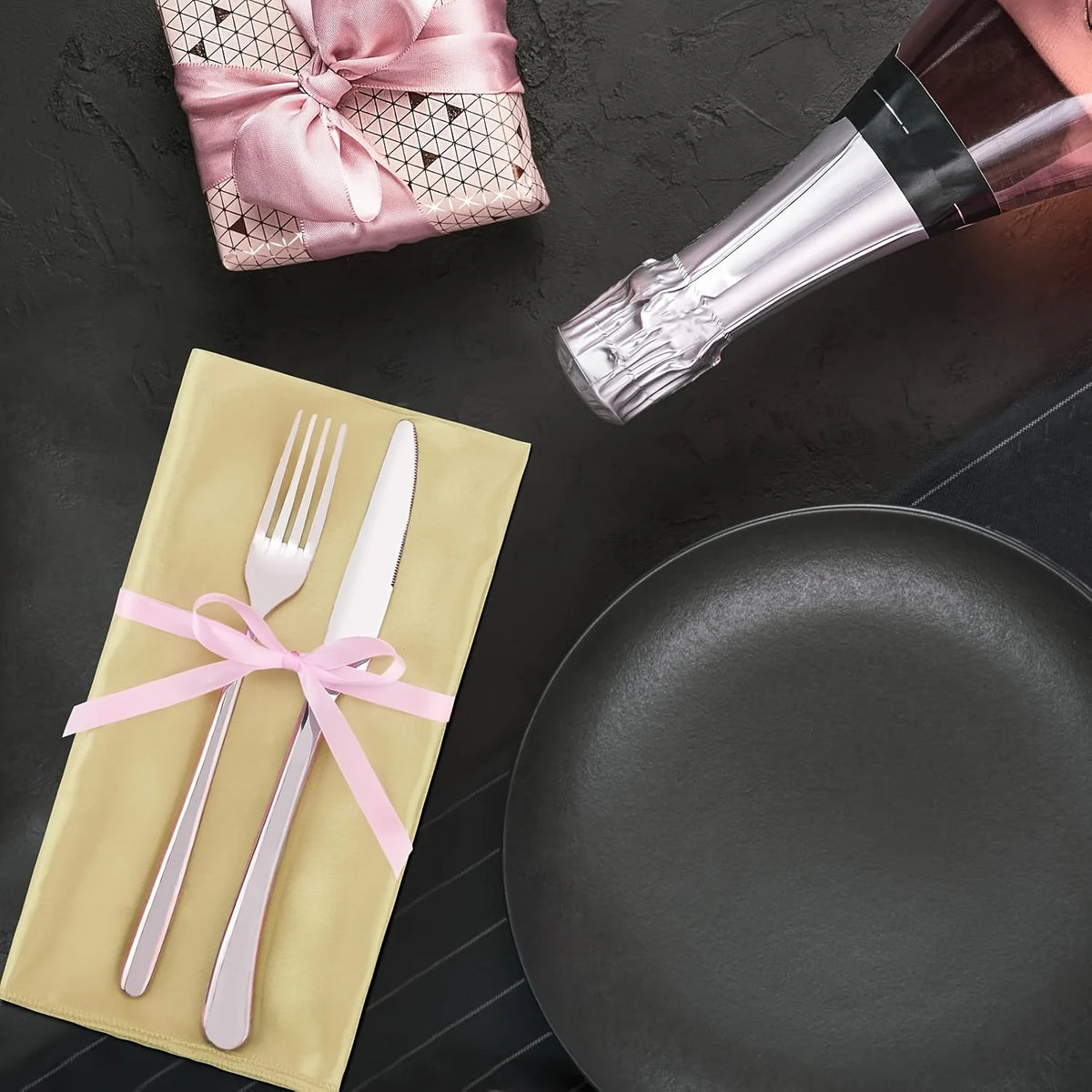 A set of pink silky satin dinner napkins and silverware are displayed on a dark surface.
