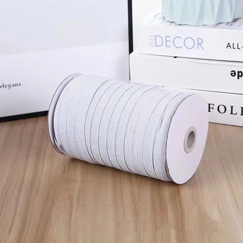 A roll of white adjustable elastic bands for garments resting on a wooden surface next to some books.