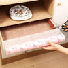 A hand is placing a pink floral reusable fridge and cabinet liner pad into a wooden cabinet shelf.