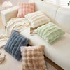 A collection of fluffy winter throw pillows in shades of pink, cream, beige, and gray arranged on a white sofa.