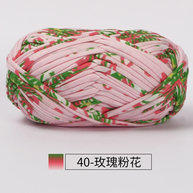 A ball of pink hand-dyed fabric strip yarn featuring a green floral pattern.