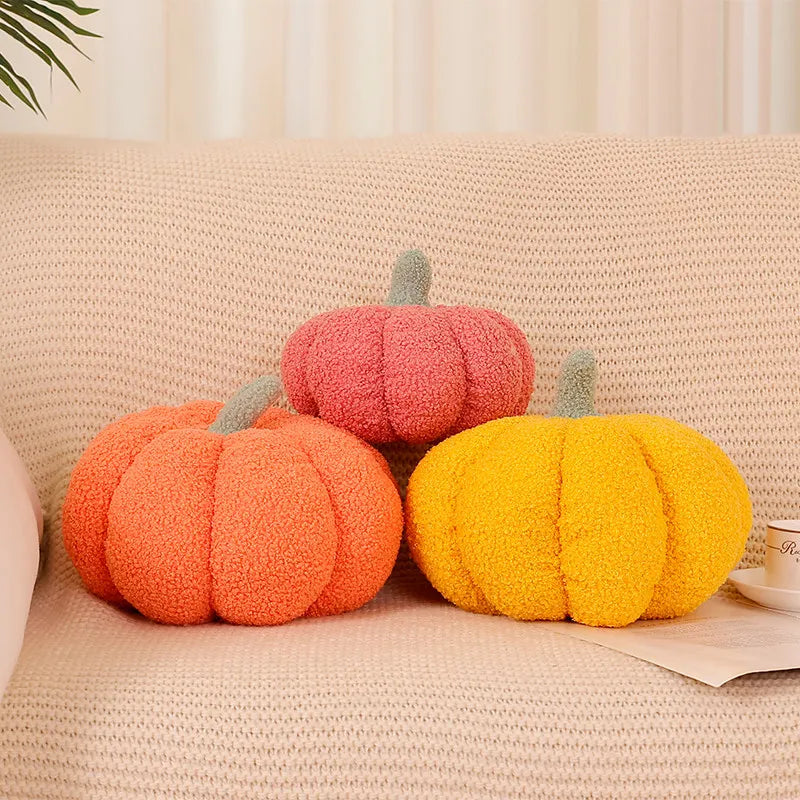 Three knitted pumpkin shaped throw pillows in shades of orange, pink, and yellow on a light beige sofa.