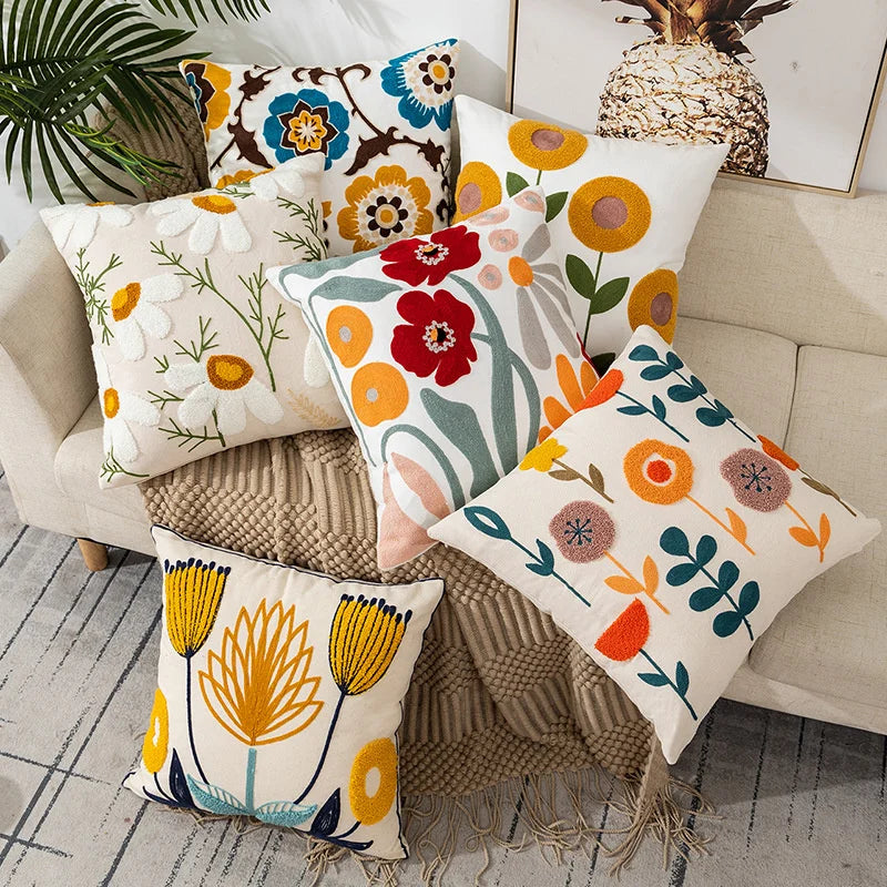 A collection of embroidered floral canvas throw pillows in various colors and patterns resting on a beige sofa.