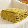 A thick, mustard yellow checkered fleece throw blanket folded neatly on a white textured surface.